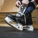 Person lacing up Bauer Supreme F40 black ice hockey skates in locker room