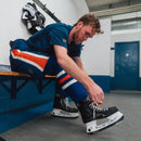 Hockey player lacing up CCM black ice hockey skates in a locker room before game.